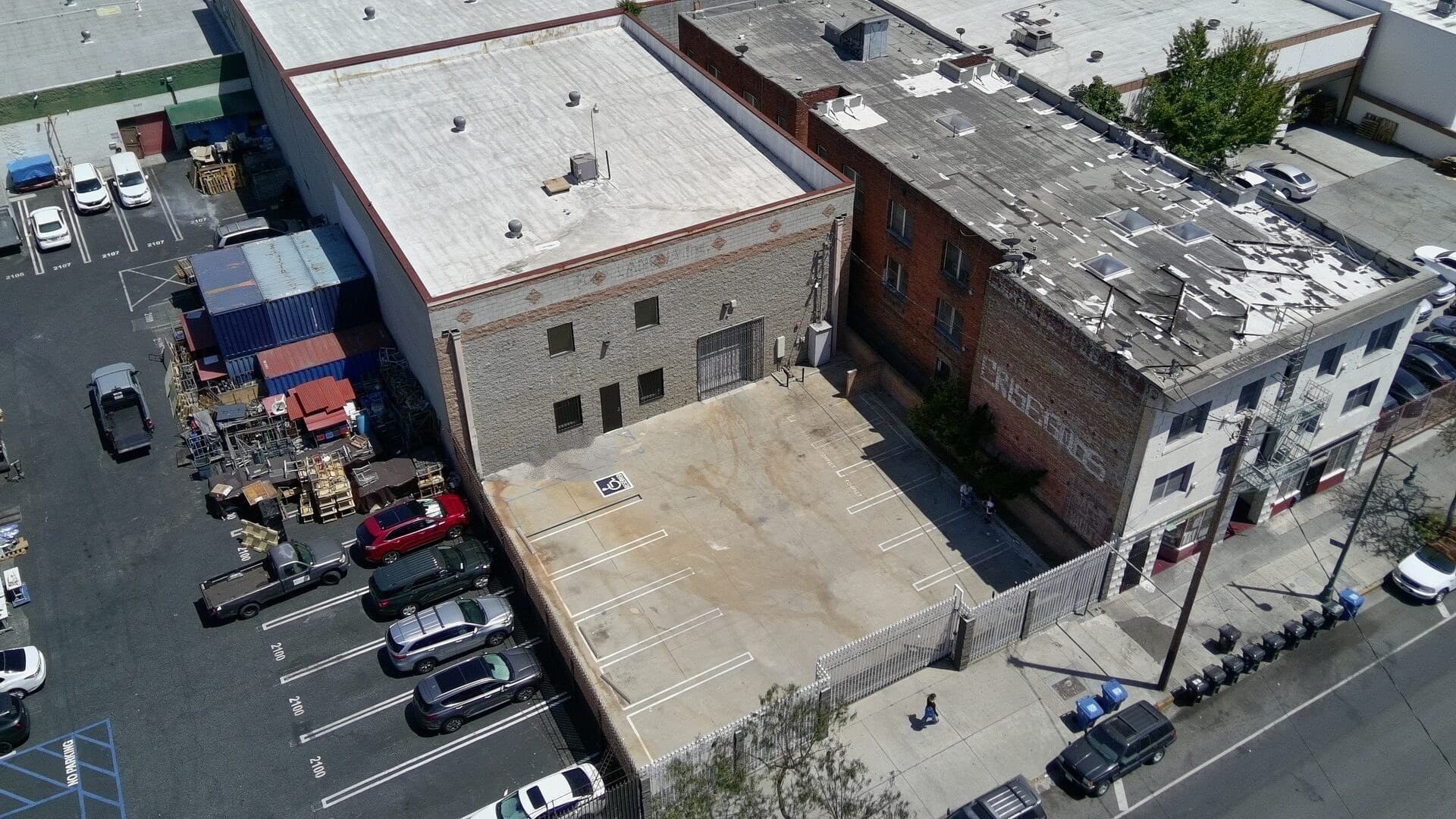 Low aerial of 2120 S Main St — standalone warehouse, white roof, and gated parking yard