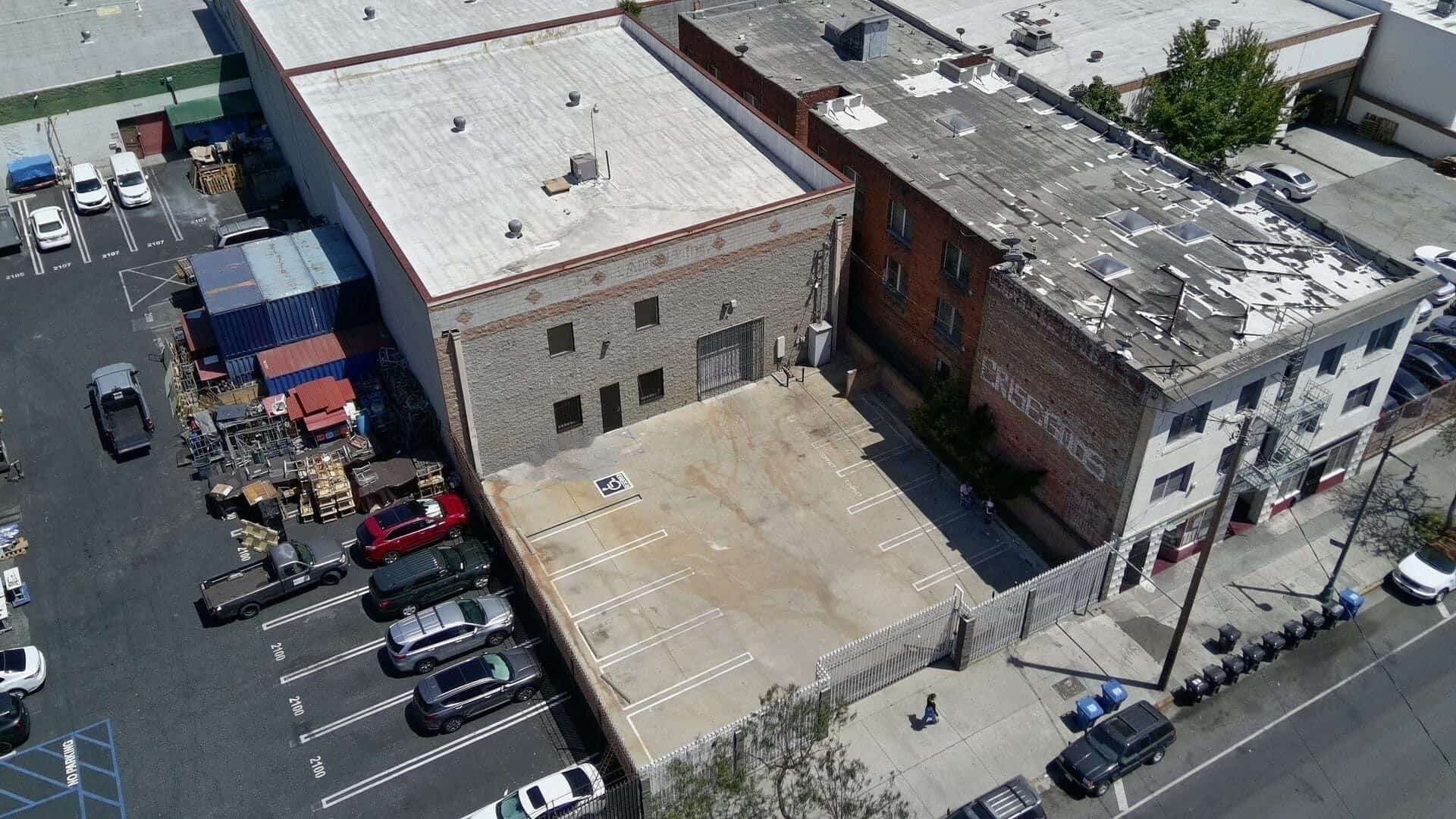 Low aerial of 2120 S Main St — standalone warehouse, white roof, and gated parking yard